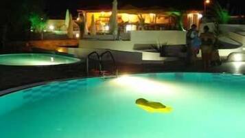 Una piscina nocturna con una silla de salvavidas y una persona de pie cerca.