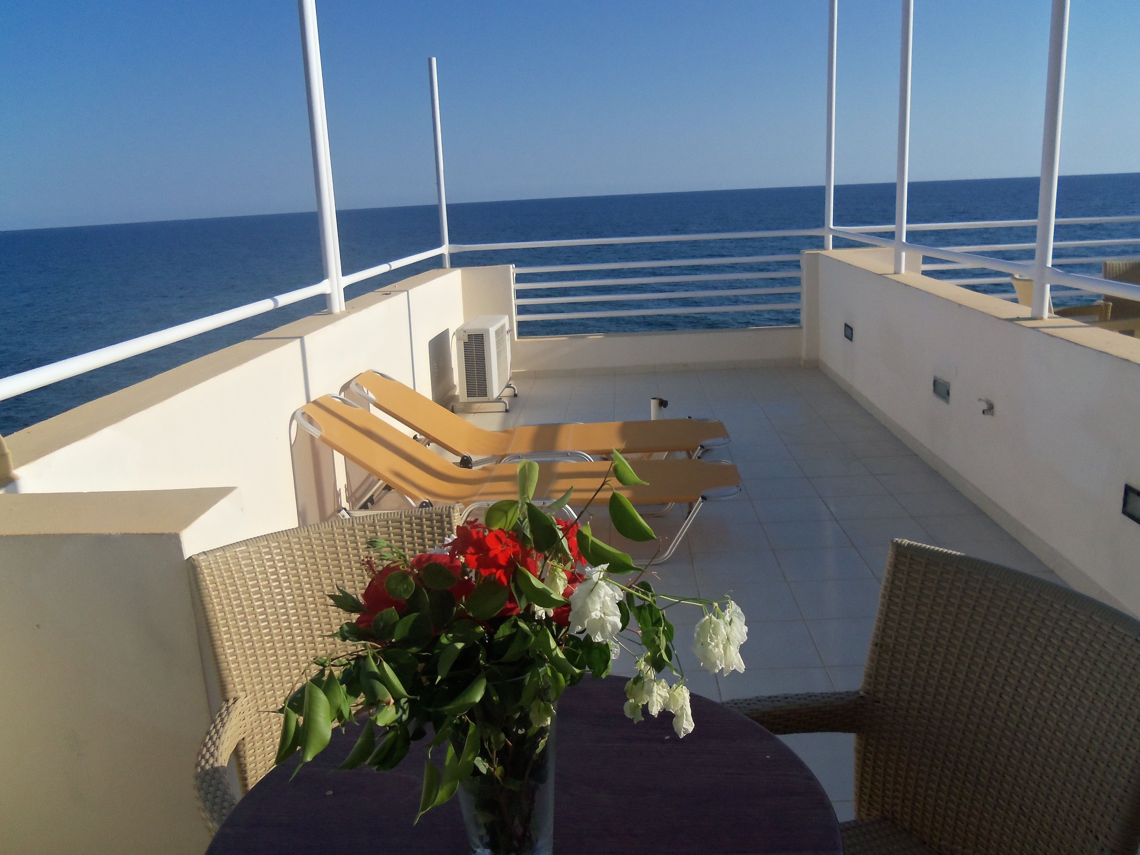 A sunlit deck with lounge chairs and a table, overlooking the sea.