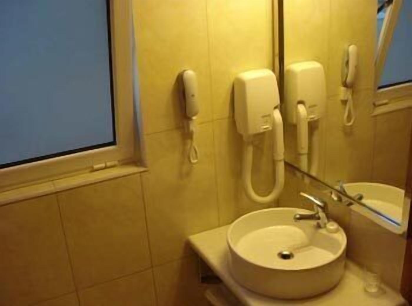 A bathroom with a sink, a mirror, and two phones mounted on the wall.