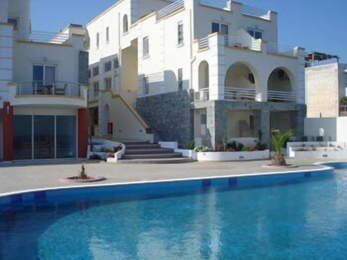 A modern building with a swimming pool, featuring multiple balconies and a central staircase.