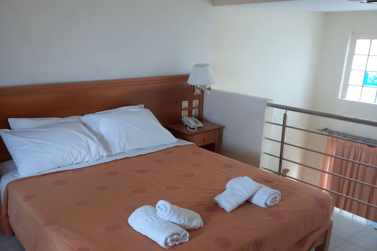 Habitación de hotel con una cama grande, una mesita de noche con lámpara y vistas al exterior a través de una ventana.