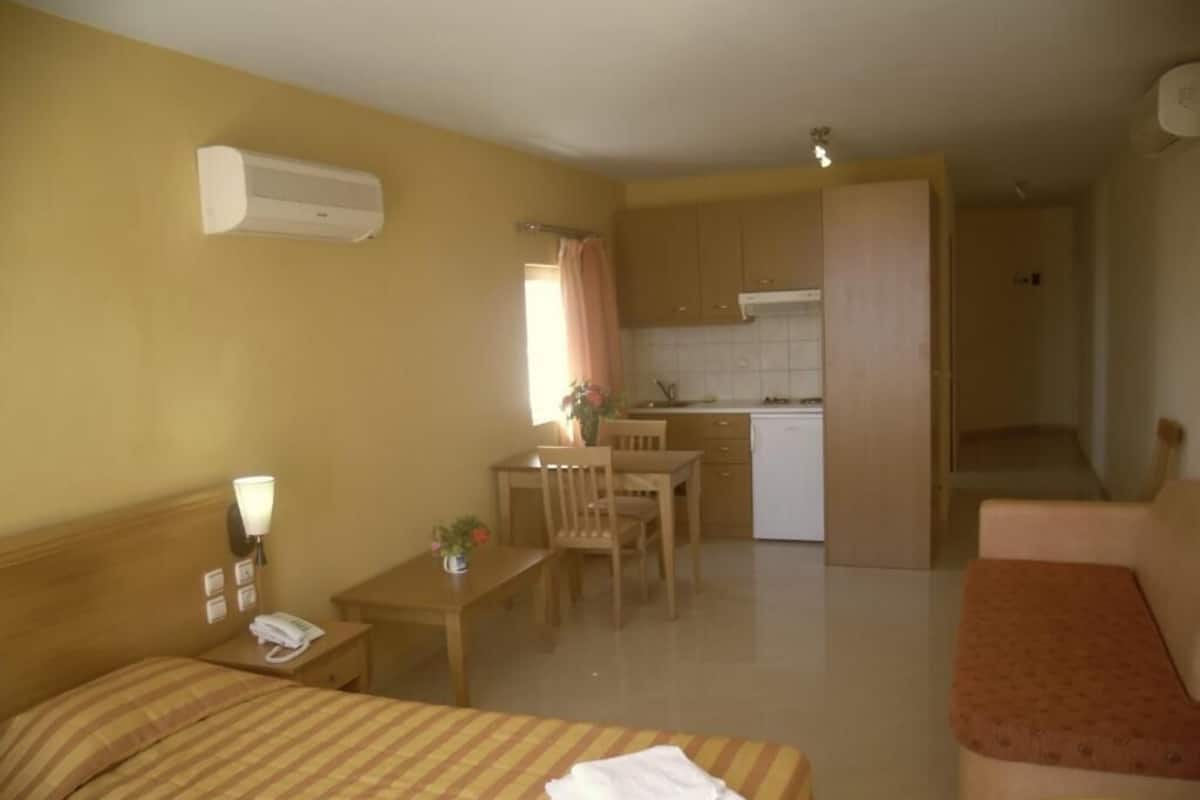 Habitación de hotel con cama, escritorio, silla, kitchenette y baño.