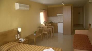 A hotel room with a bed, a desk, a chair, a kitchenette, and a bathroom.