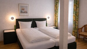 A double bed with two pillows, a nightstand, a wall-mounted lamp, a framed picture, and a chair. - Klusenhof (Lippstadt)