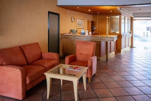 A hotel lobby with a sofa, armchair, and a small table with a magazine.