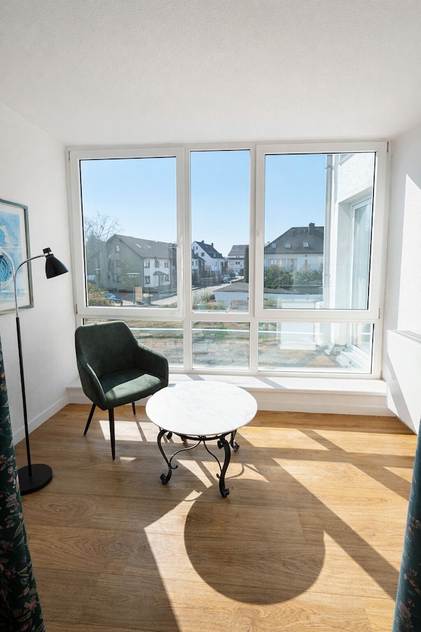 A room with a large window, a green chair, a white table, and a floor lamp.