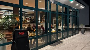 A restaurant with outdoor seating, a Coca-Cola sign, and a neon sign above the entrance. - Klusenhof (Lippstadt)
