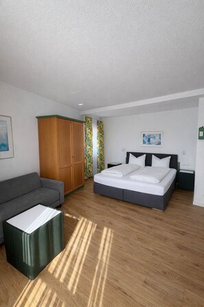 A modern hotel room with a bed, a sofa, a wardrobe, and a small table. - Klusenhof (Lippstadt)