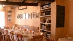 Een eetgedeelte met houten wanden, een lange tafel gedekt voor meerdere gasten, en een boekenkast vol boeken en flessen.