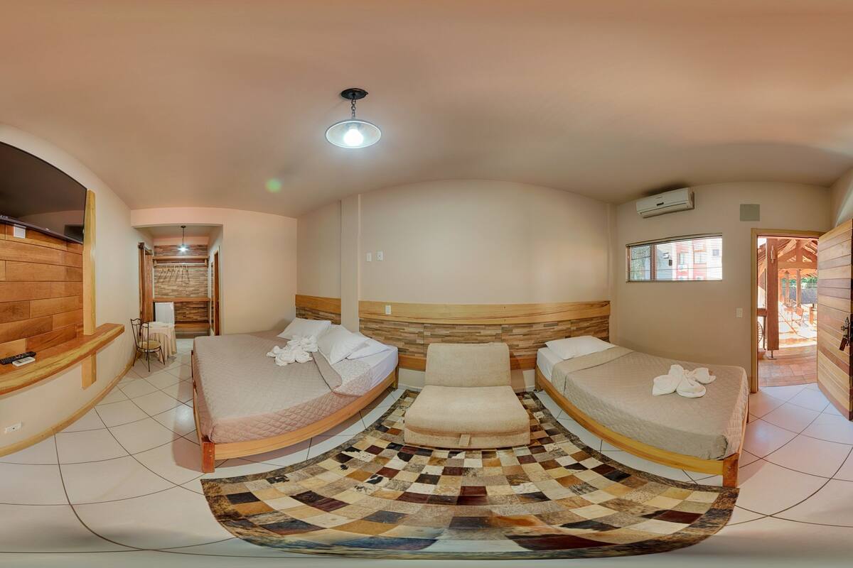 A room with a curved bed, a flat-screen TV mounted on a wooden wall, a ceiling light, and a window with a view.