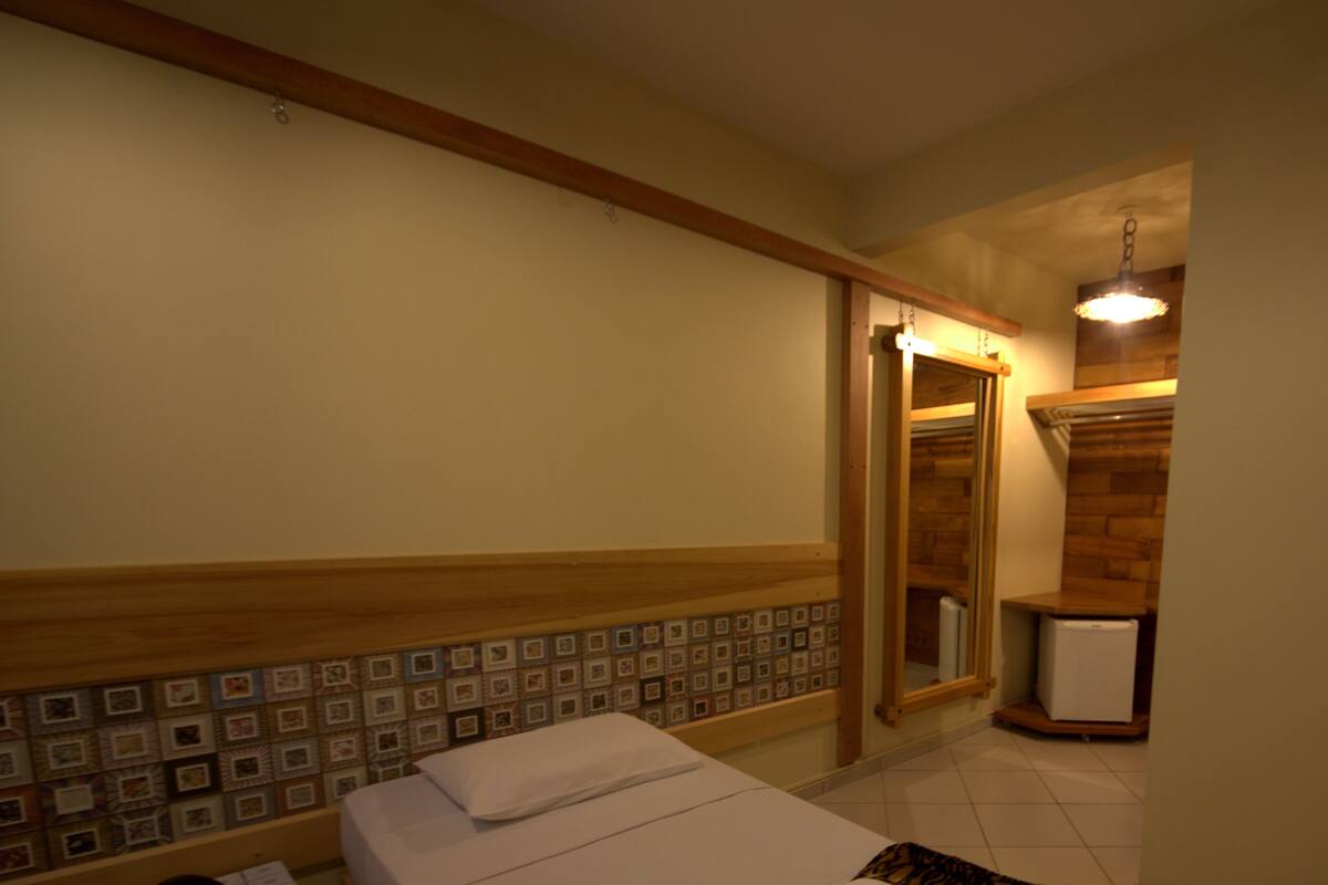 A hotel room with a bed, a small table with a remote control, and a mirror.