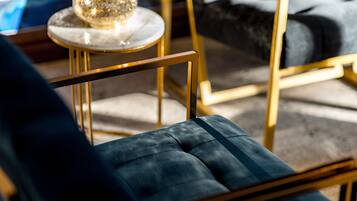 Una silla moderna con estructura dorada y cojín azul oscuro, ubicada cerca de una pequeña mesa redonda con tapa de mármol y un objeto de vidrio decorativo.