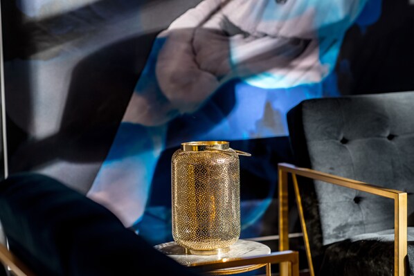 A decorative lamp on a table, a tufted chair, and a large abstract painting in the background.