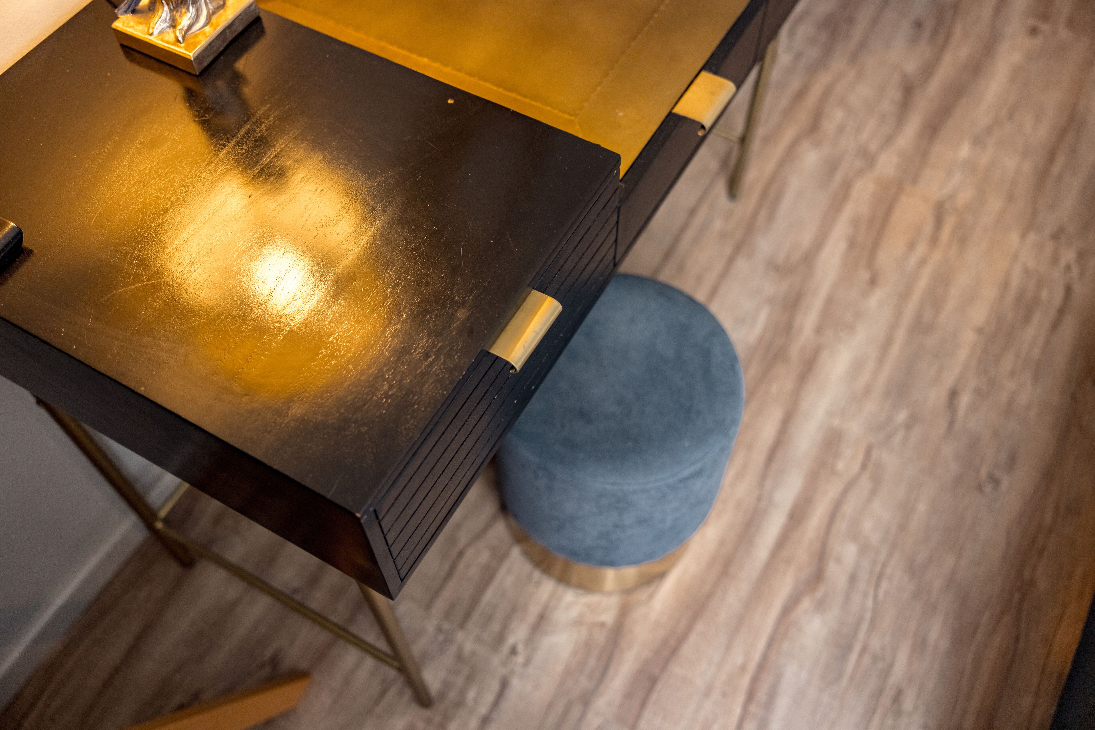 Une table en bois avec un plateau doré et un pouf rond bleu placé à côté.