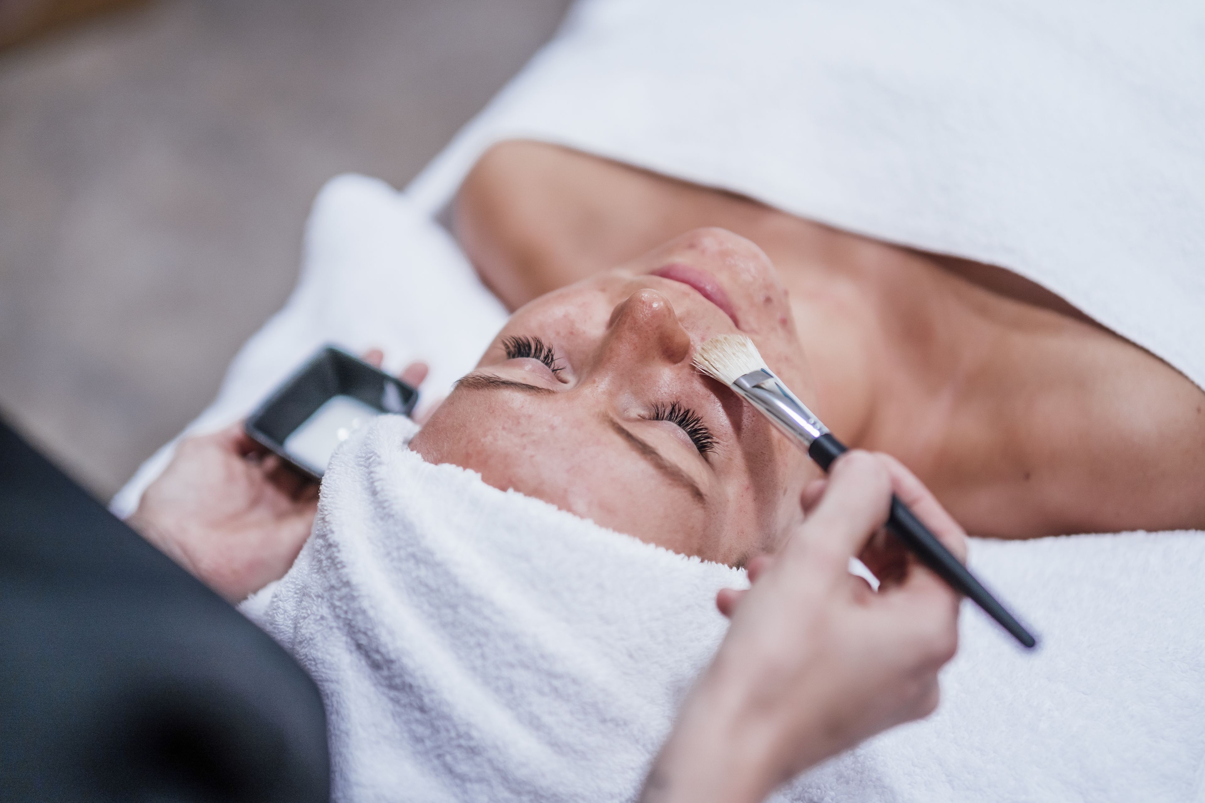 Una persona acostada con una toalla en la cabeza, recibiendo un tratamiento facial.