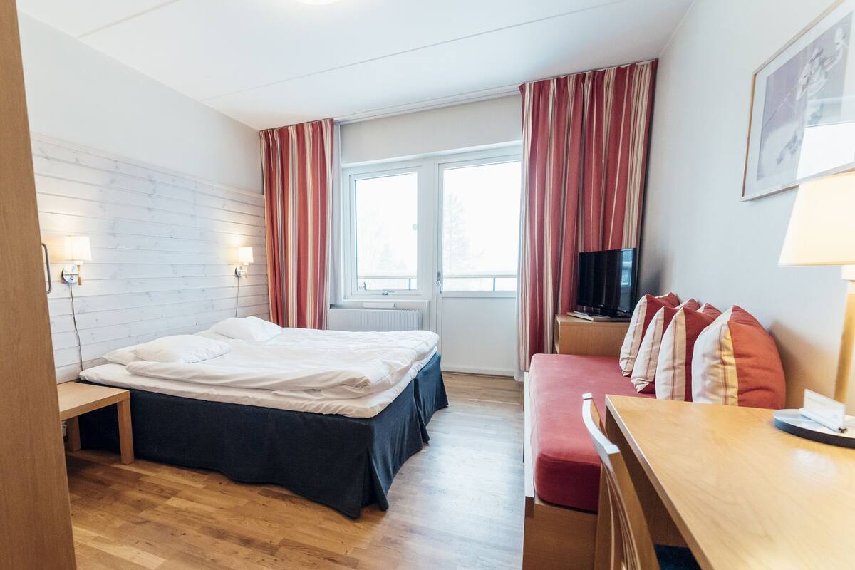 A hotel room with a bed, a desk, a TV, and a window.