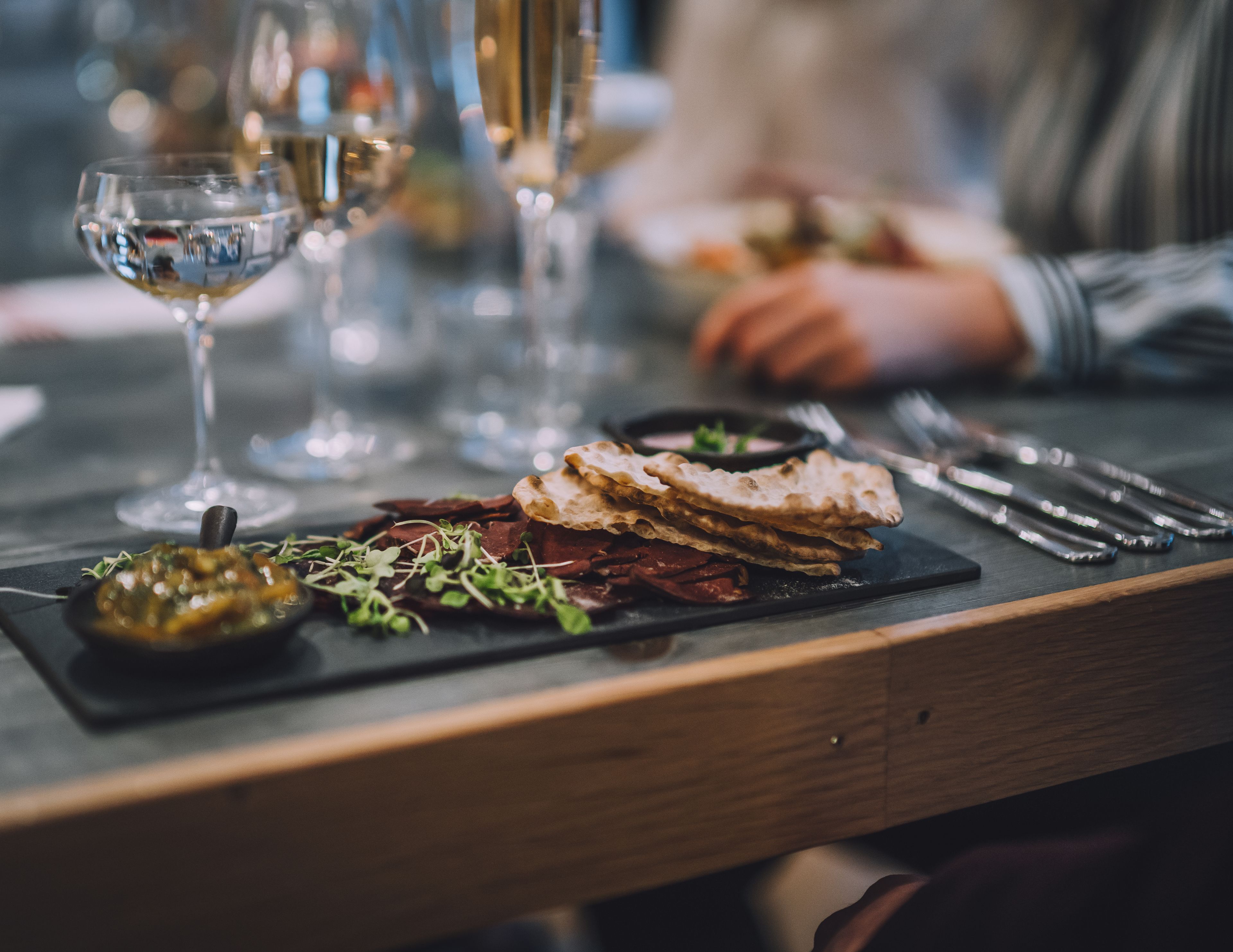 Ett matbord med en svart skifferplatta som används som serveringsyta och som innehåller ett urval av matvaror, inklusive bröd, grönsaker och en liten skål med sås.