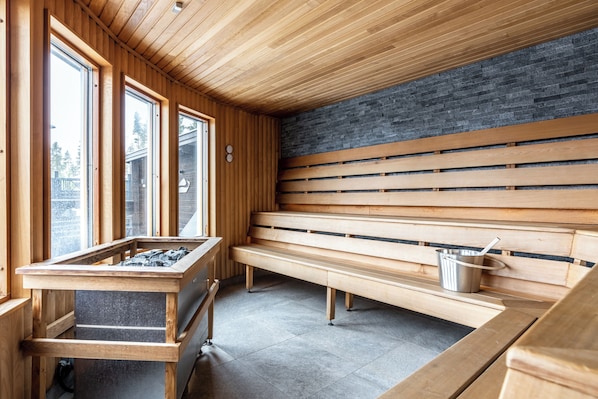 Un sauna avec des bancs en bois, un mur en pierre et de grandes fenêtres.