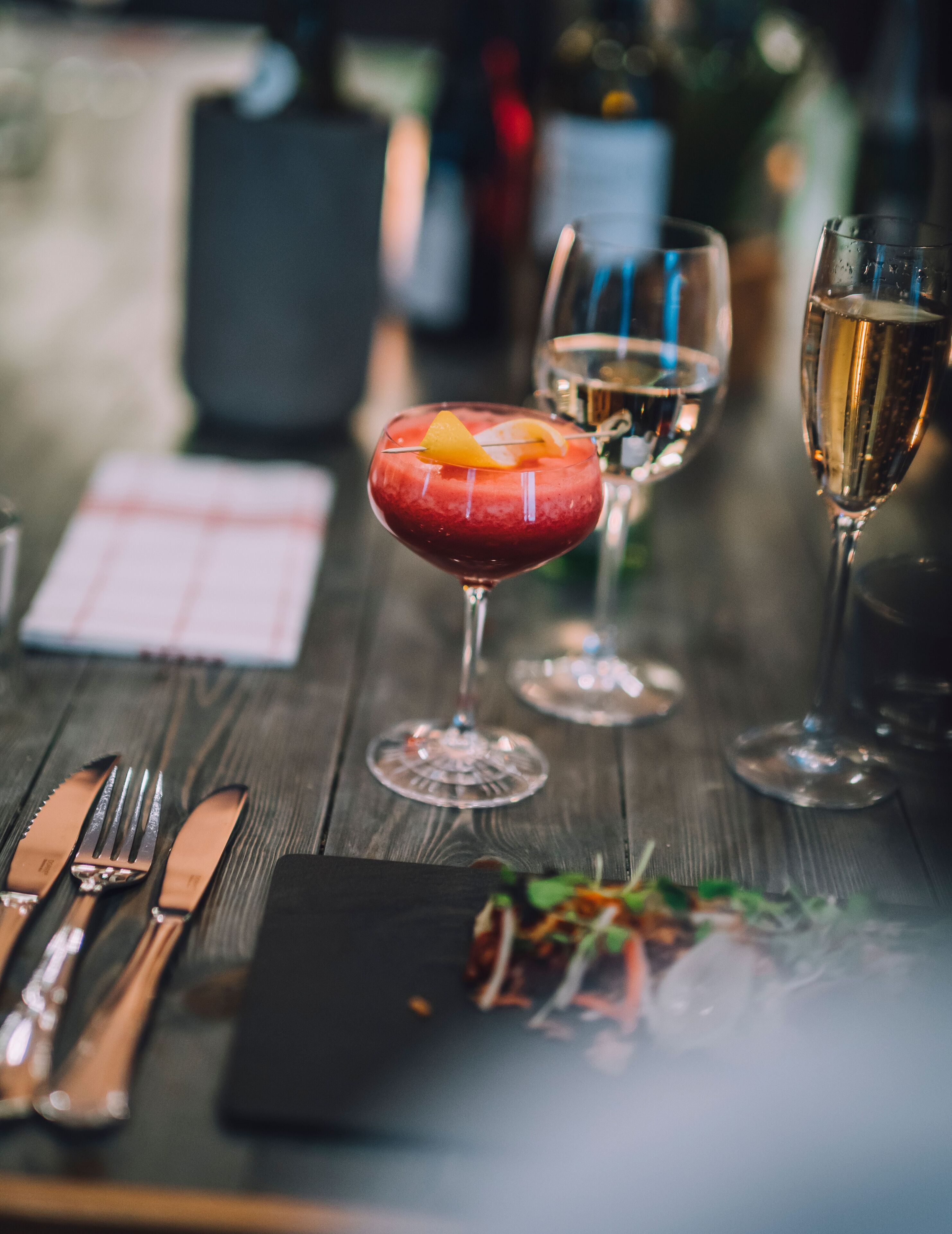Una mesa de comedor con un cóctel rojo, una copa de vino blanco y una copa de champán.