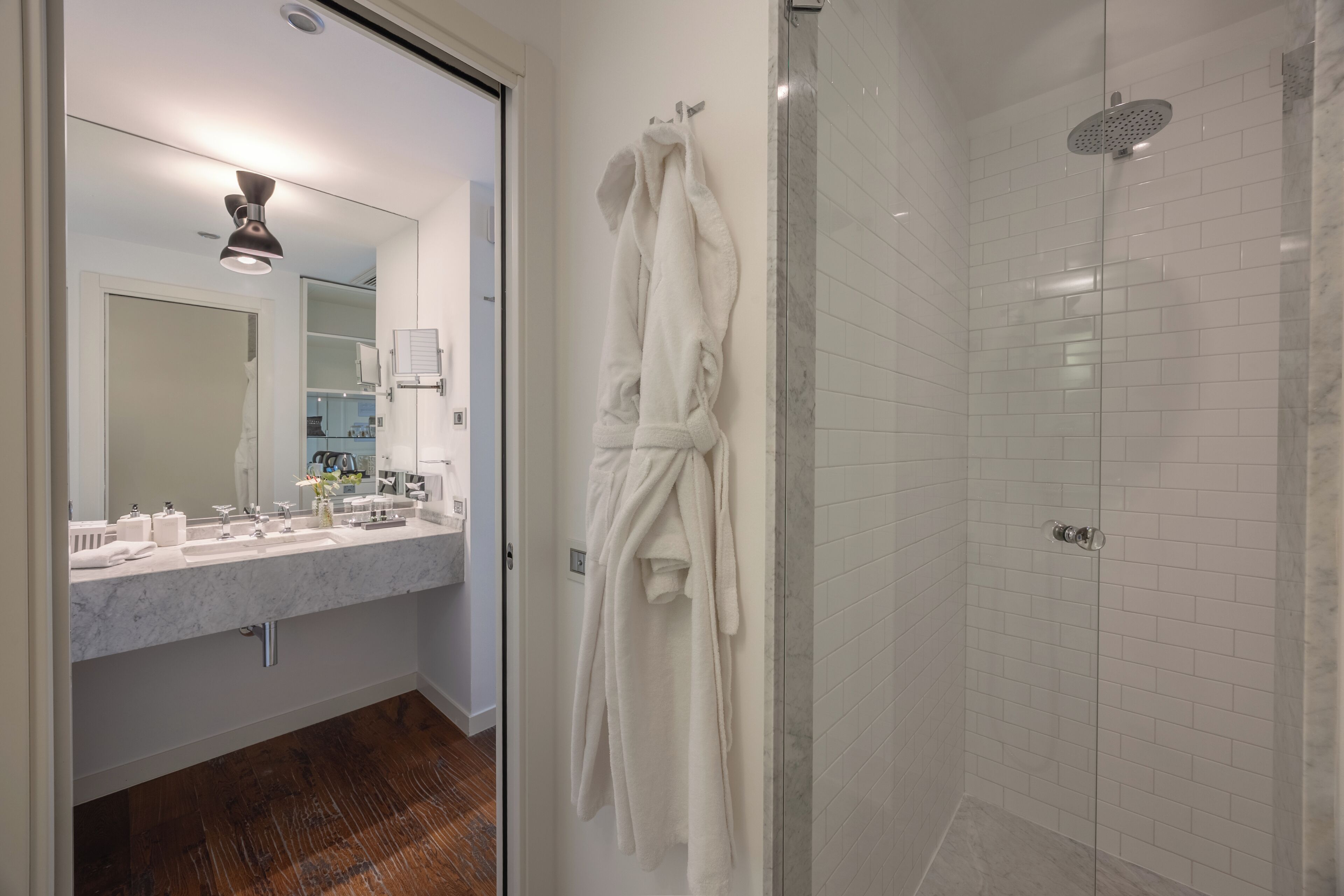 Un baño moderno con lavamanos de mármol, cabina de ducha de vidrio y una bata blanca colgada en la pared.