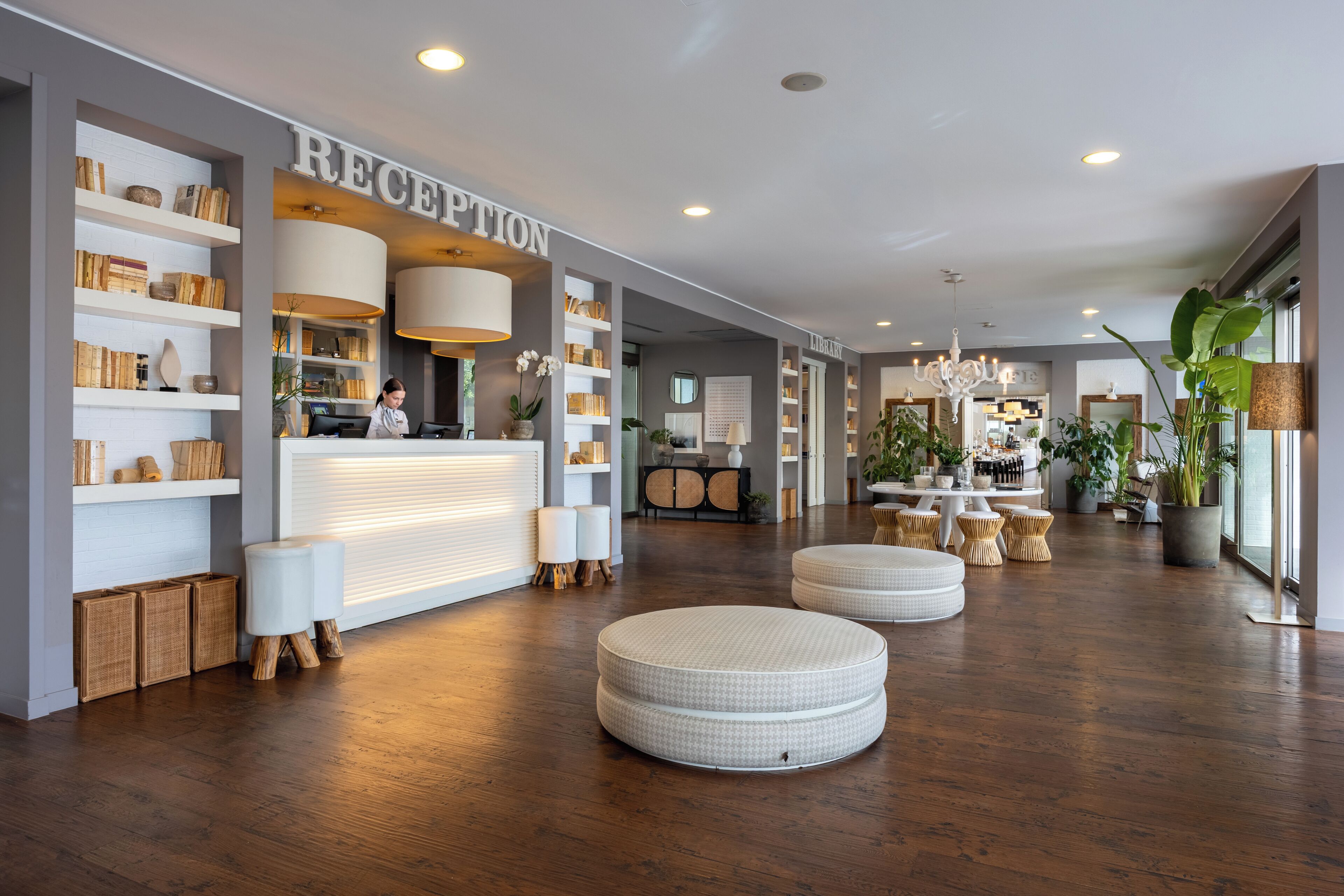 A reception area with a reception desk, shelves with books and decorative items, round white ottomans, and a wooden floor.