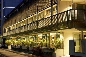 A modern hotel facade with horizontal slats, large windows, and potted plants along the ground floor.