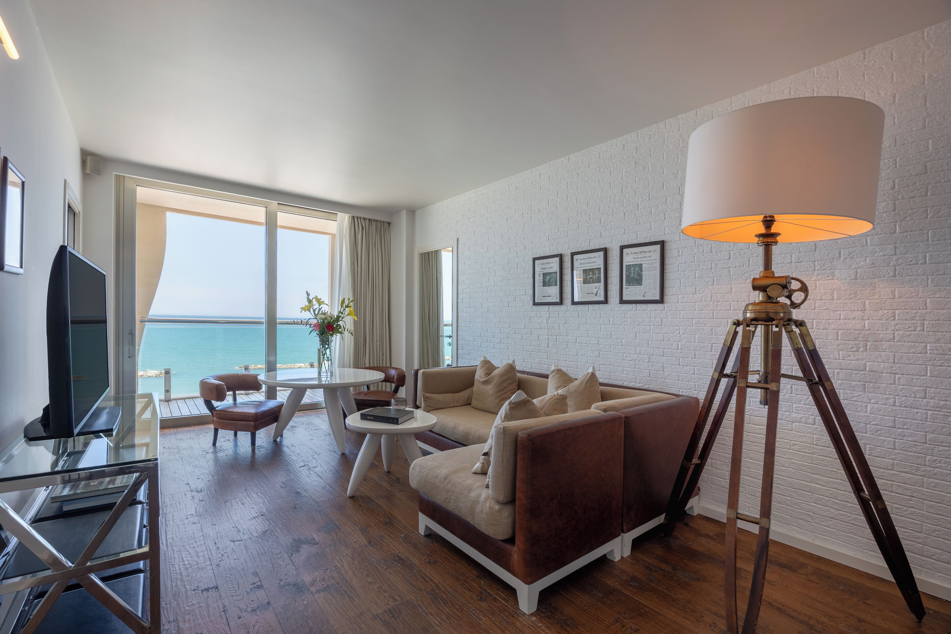 Un salon moderne avec un canapé, une table basse et un téléviseur. Une grande fenêtre offre une vue sur la mer.