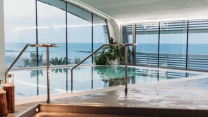 Un área de piscina interior moderna con barandillas de vidrio y vista al océano.