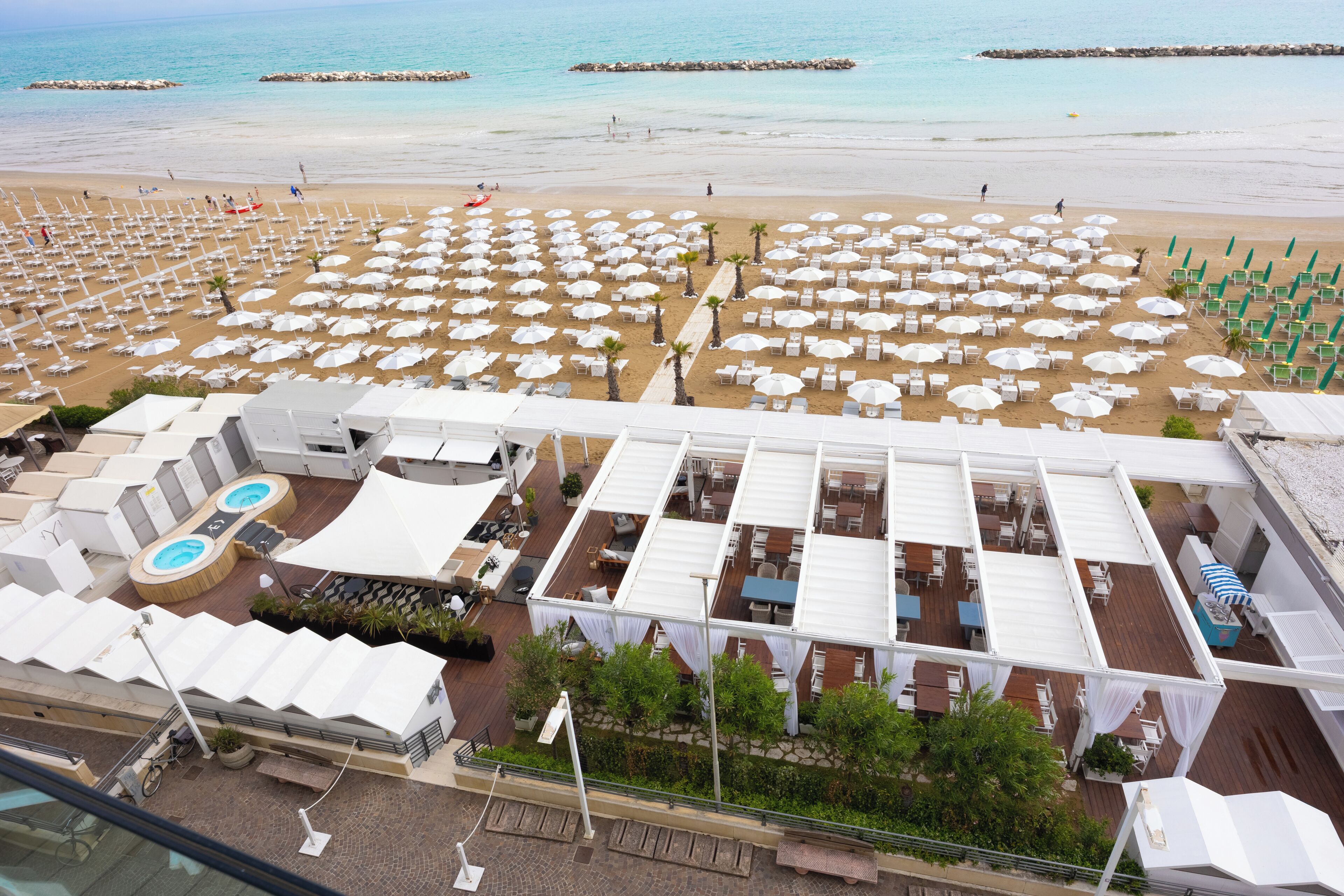 A beach resort with multiple white umbrellas, sun loungers, and a pool area.