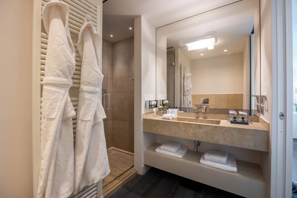 A modern bathroom with a walk-in shower, a large mirror, and neatly folded towels on shelves.