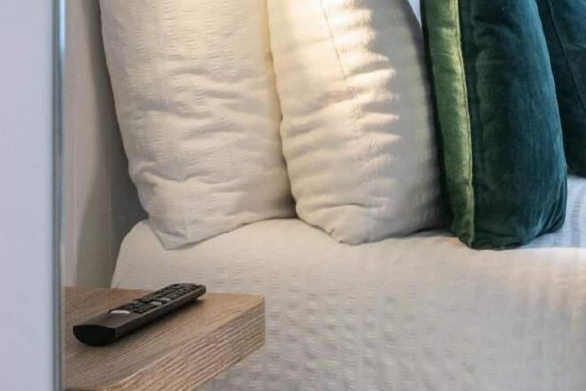 Un lit avec des oreillers et une télécommande posée sur une table de chevet en bois.