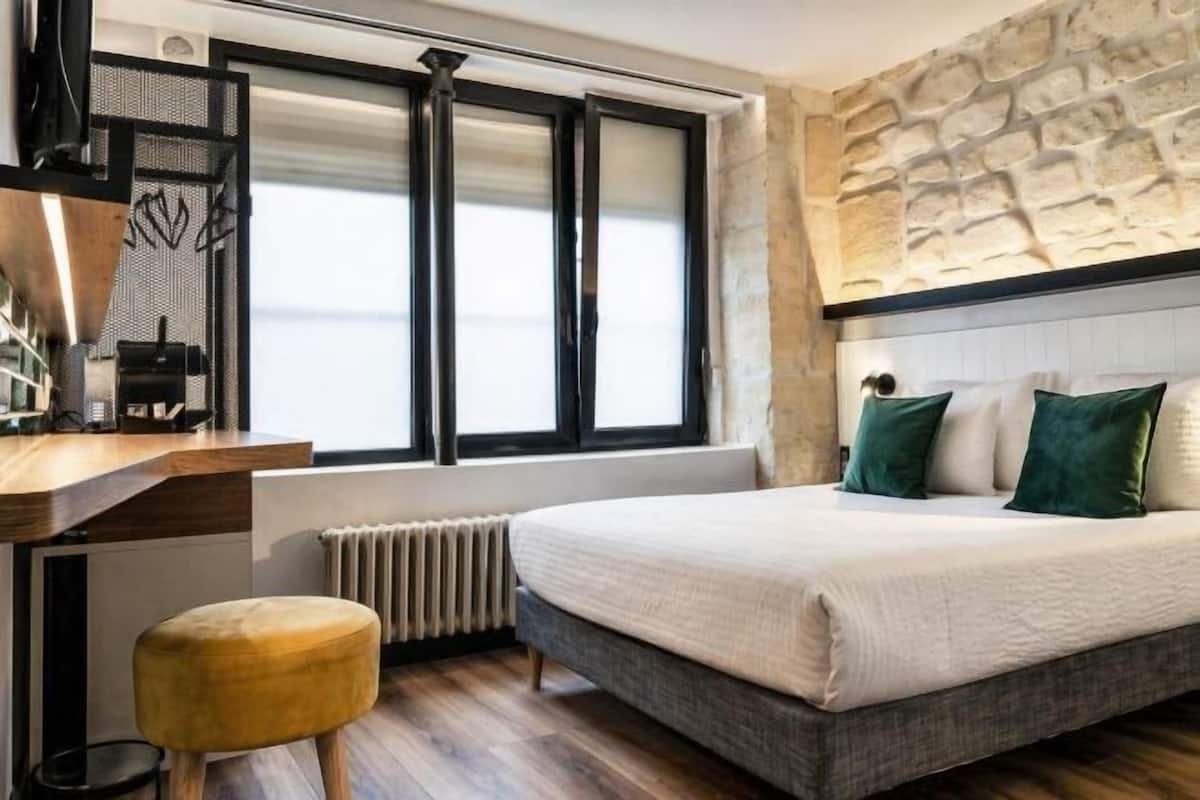 Une chambre avec un lit, un bureau, un radiateur et un mur en pierre.