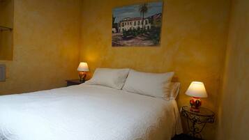 A bed with white linens, two bedside lamps, and a painting on the wall.