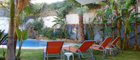 A poolside area with a small waterfall, surrounded by lush greenery and a white canopy.