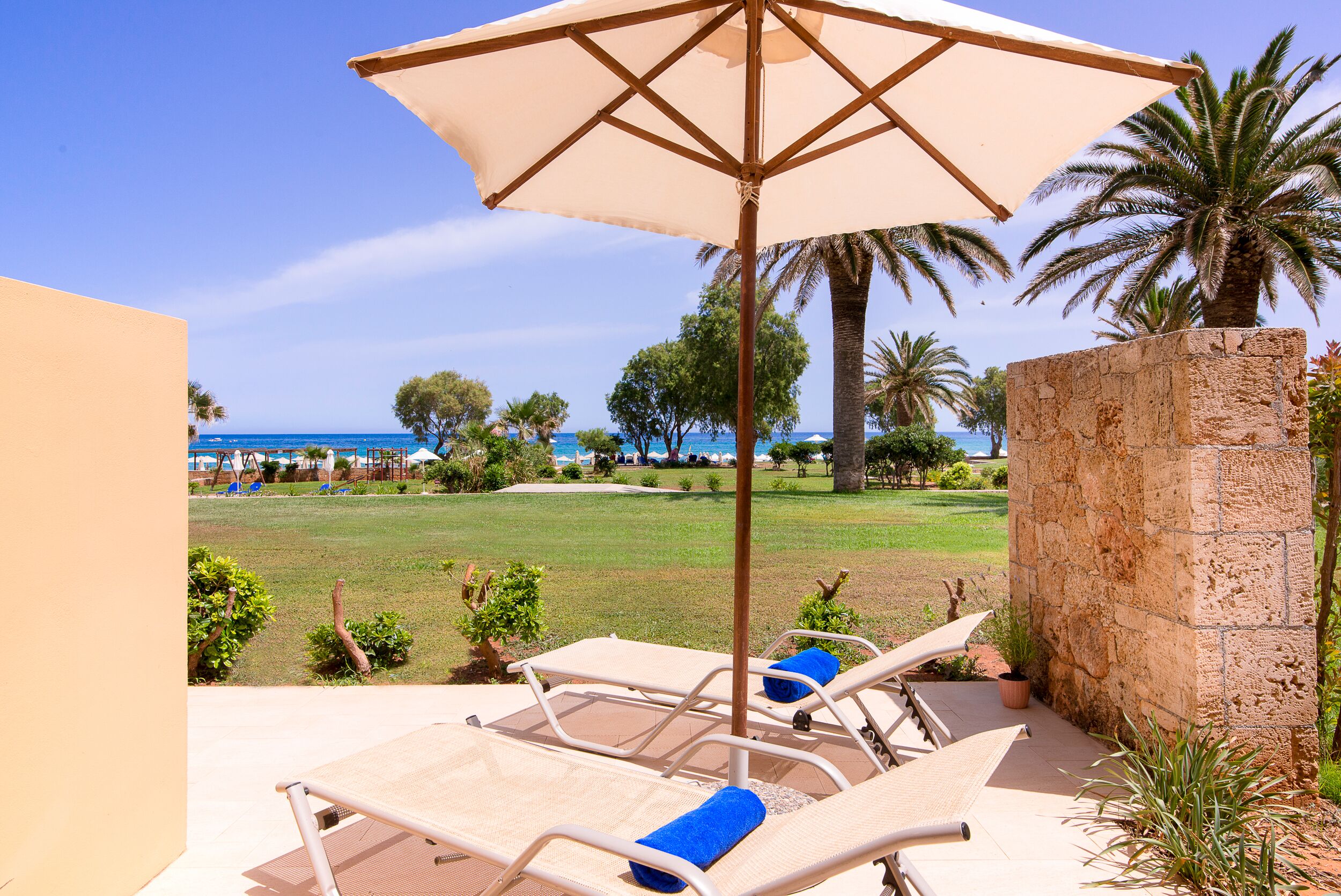 Un salon de plage doté d’un grand parasol, de chaises longues et offrant une vue sur la mer et les palmiers.
