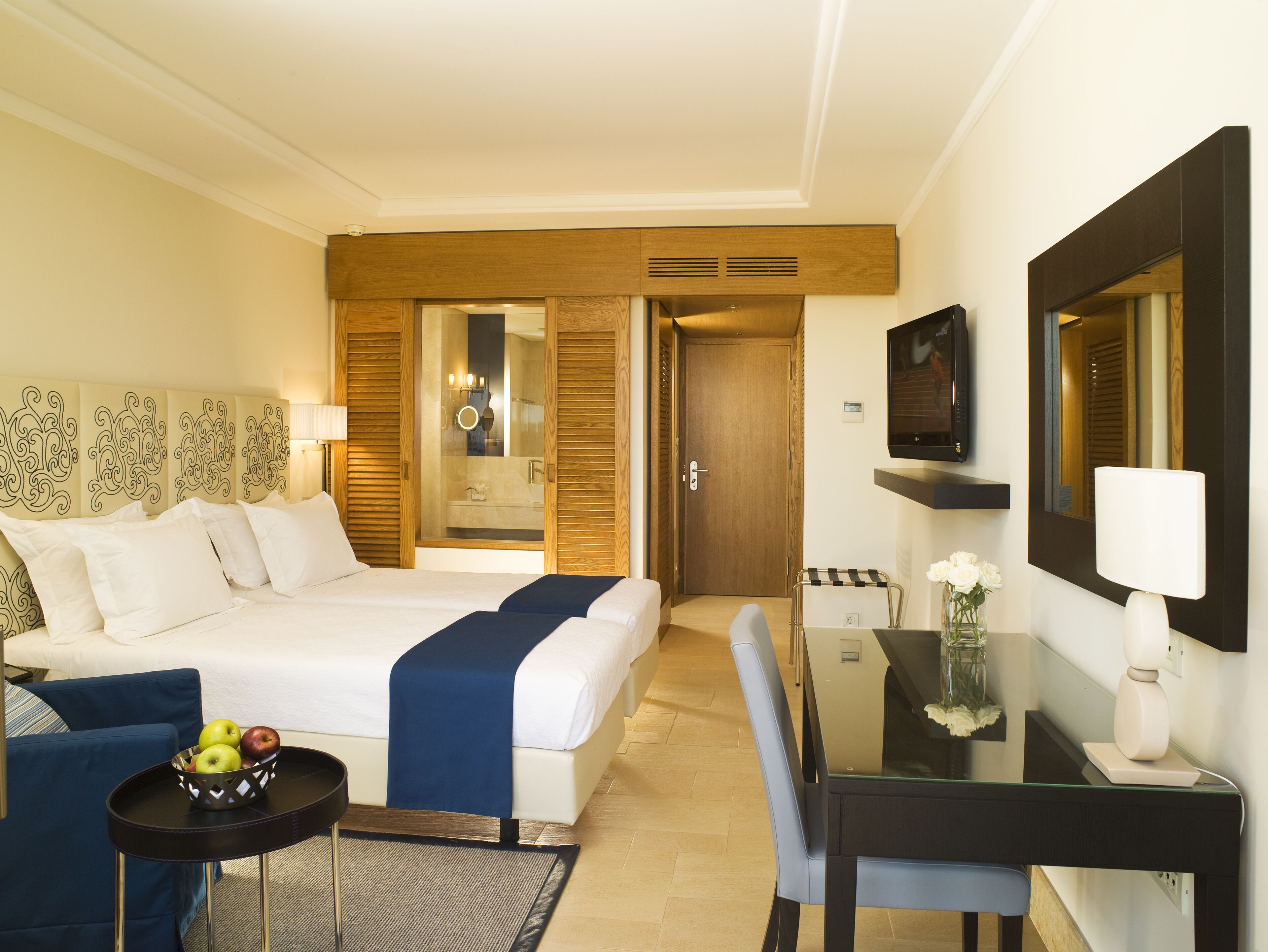 Habitación de hotel con cama, mesita de noche, silla, escritorio y televisor.