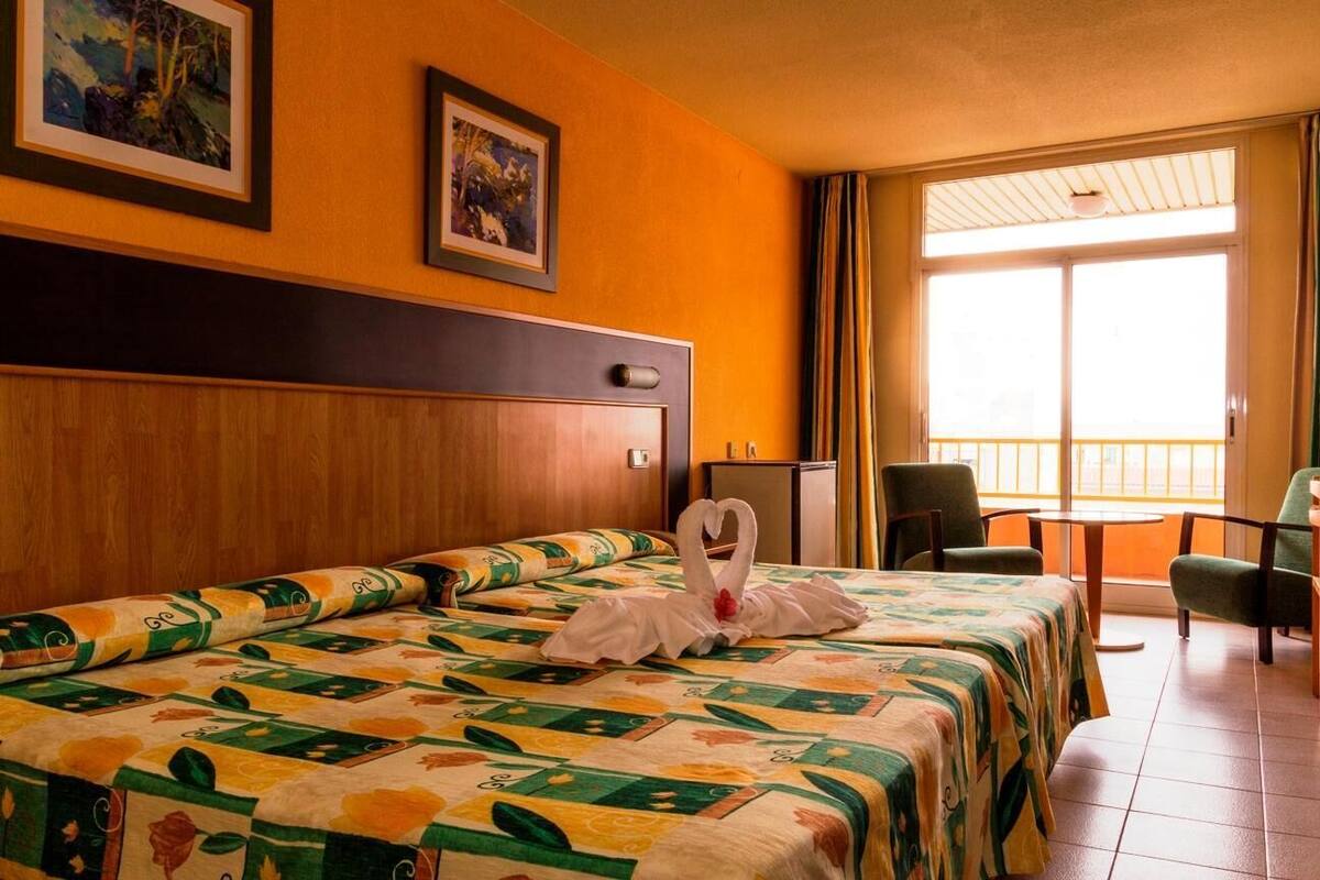 A hotel room with a large bed, a wooden headboard, a balcony with chairs, and two framed pictures on the wall.