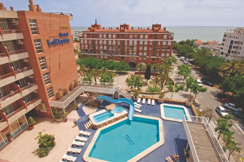 Ein Hotel mit mehreren Schwimmbecken, Blick auf den Strand und einem rotbackigen Gebäude.