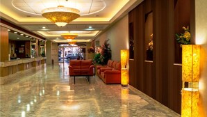 Eine Hotelhalle mit Marmorboden, einer Rezeption, zwei Sofas und einer großen Kandelaber.