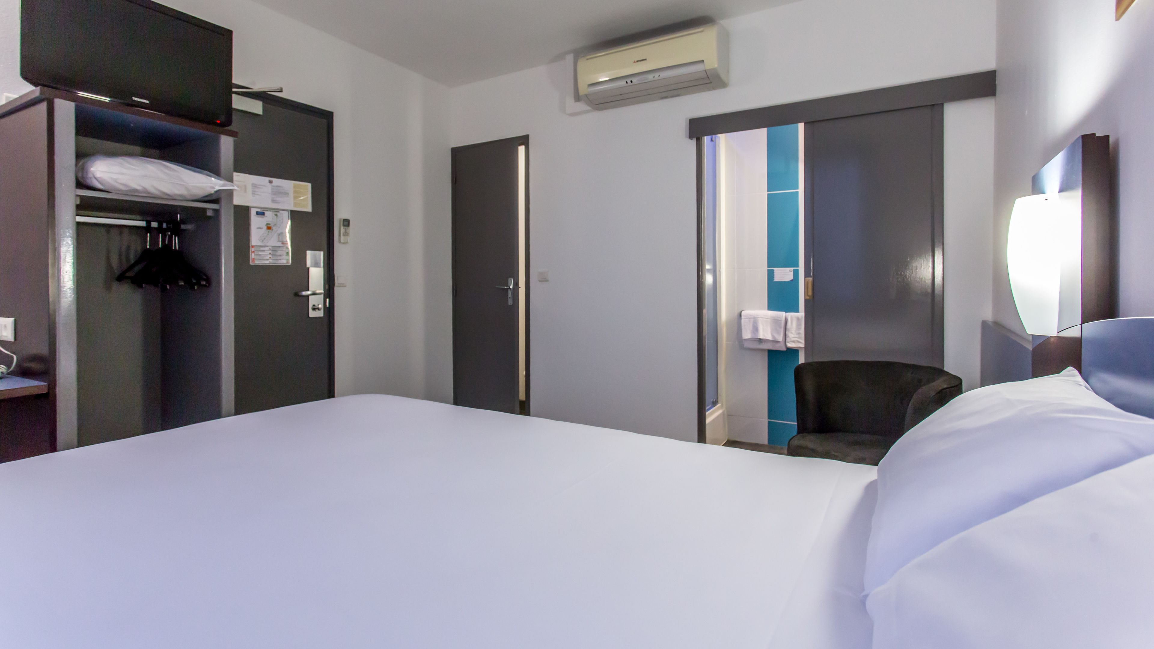 Una habitación de hotel con cama, armario, silla y escritorio con lámpara.