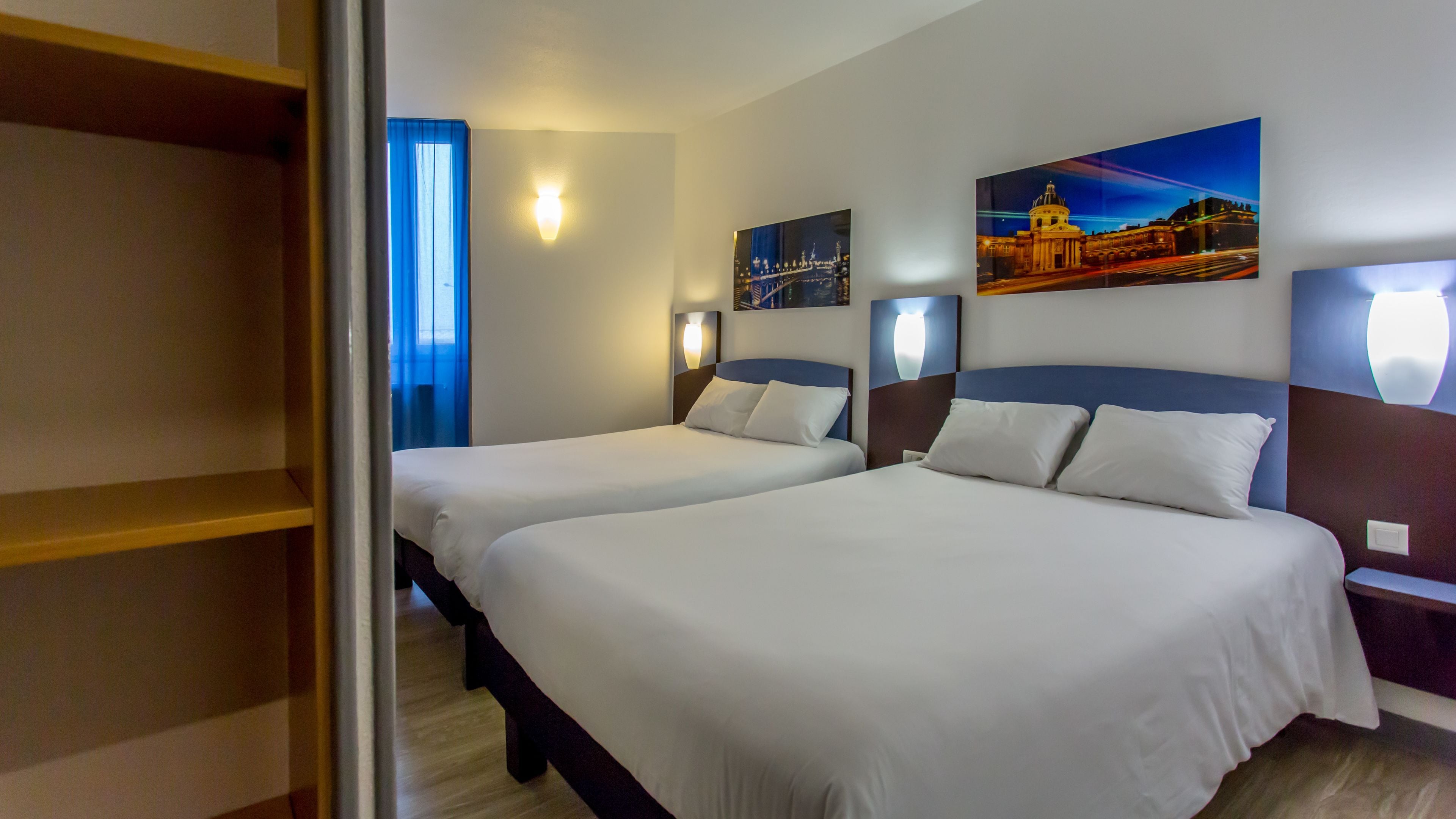 Una habitación de hotel con dos camas, un armario y obras de arte en las paredes.