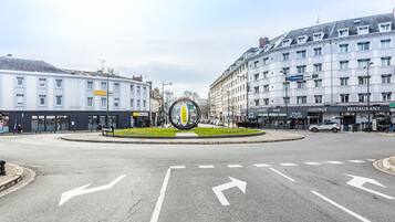 A roundabout with a central island featuring a yellow and green sign. Surrounding buildings include a hotel with a sign for "Longmaine Hotel" and a building with a sign for "Made in Late."