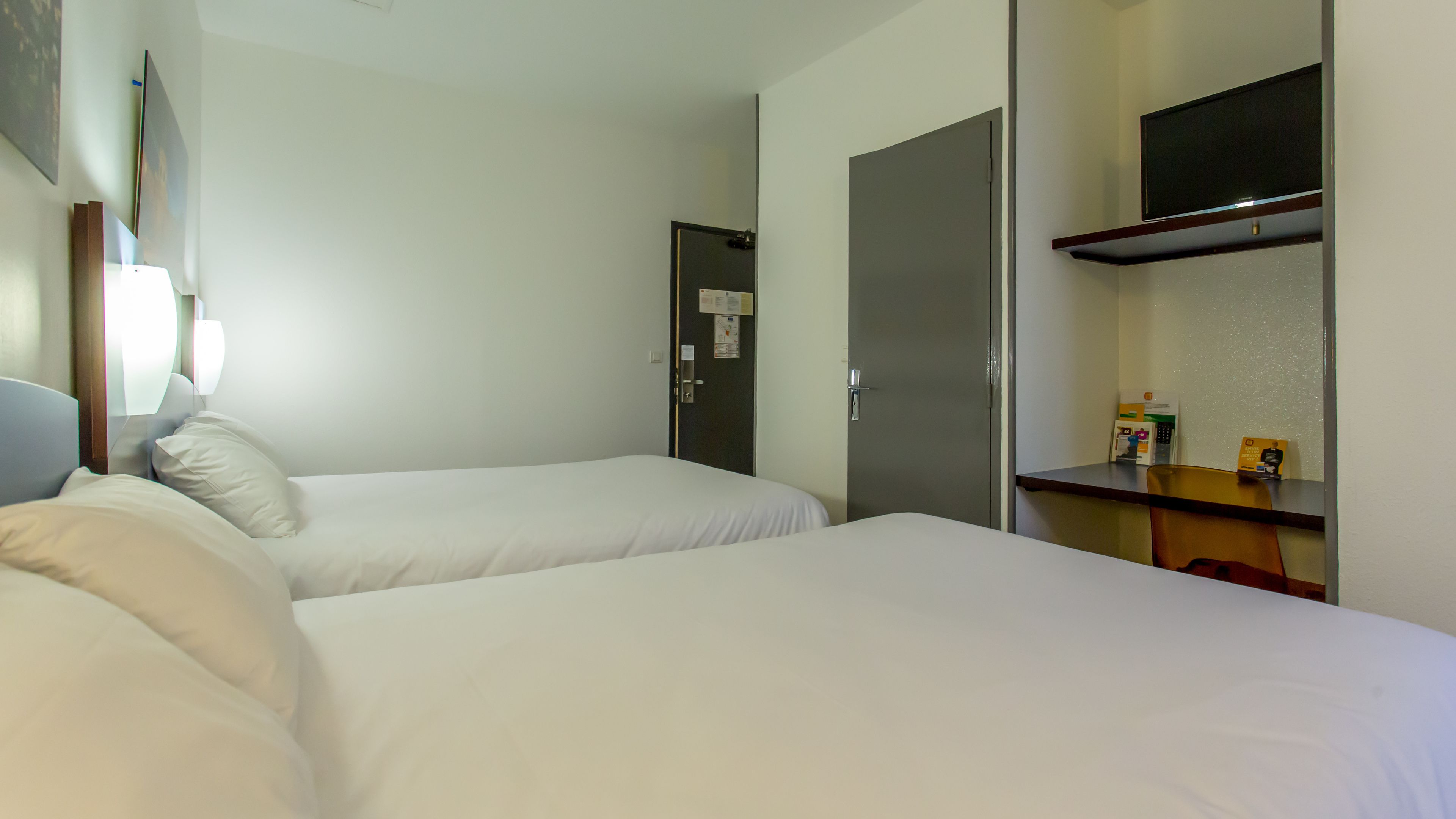 Habitación de hotel con dos camas, un escritorio, una silla, un televisor y un armario.