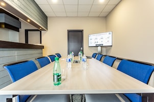 A conference room with a long table, blue chairs, water bottles, and a presentation screen.