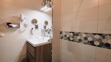 A bathroom with a white sink, wooden vanity, and a mirror. There is a towel rack and a soap dispenser on the wall.