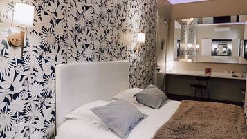 A hotel room with a bed, a nightstand, a mirror, and a bathroom visible through an open door.