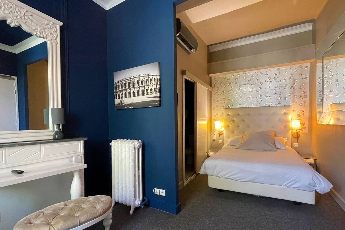 Un dormitorio con cama, cómoda, espejo, radiador y un cuadro de un edificio en la pared.