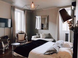 A bedroom with a bed, a chair, a table, a mirror, and a lamp.