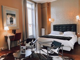 A hotel room with a bed, a desk with a chair, a table, and a cowhide rug.