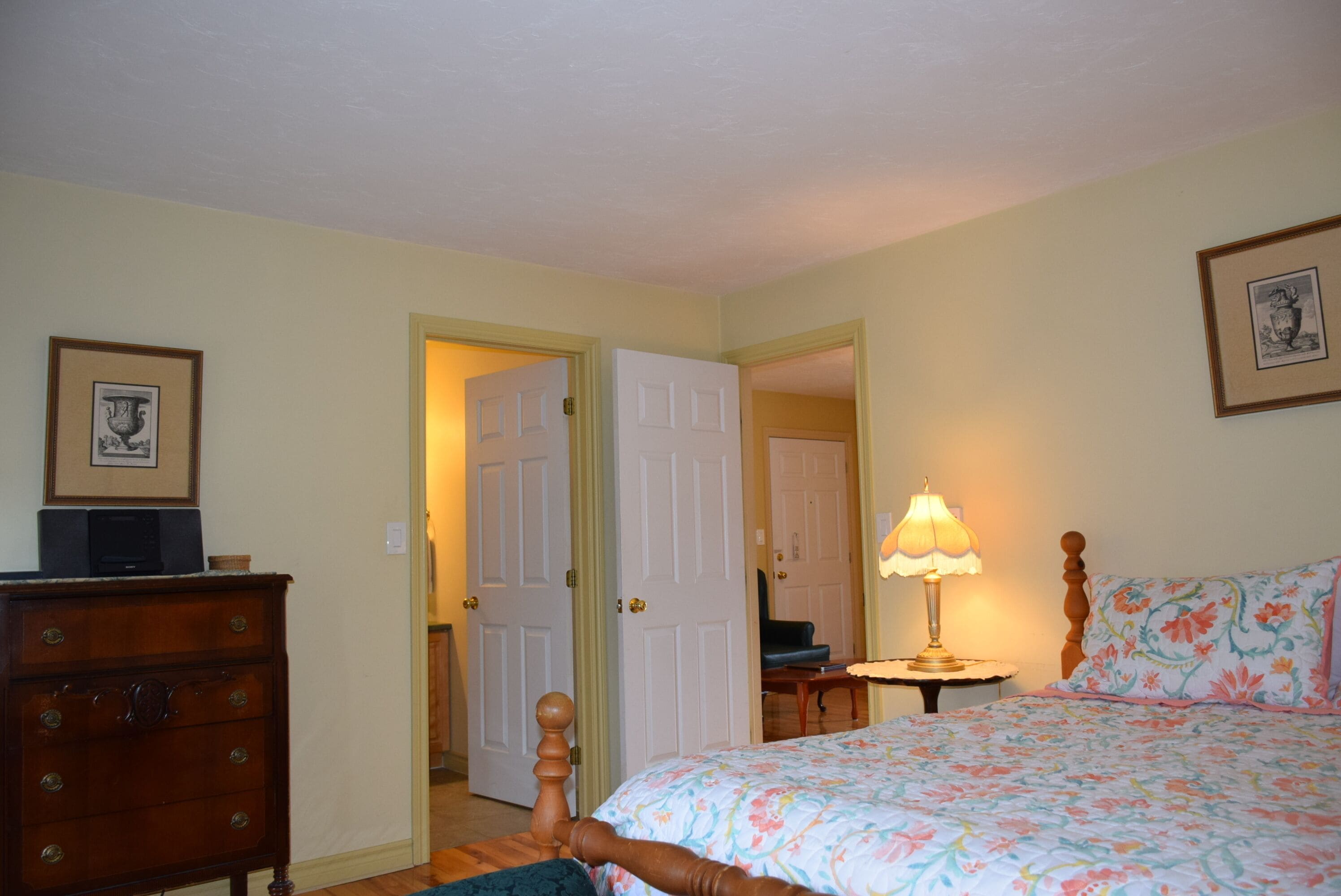 Une chambre à coucher avec un lit, une commode, une lampe et un tableau encadré au mur.